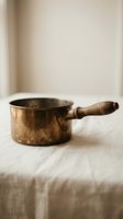 Vintage copper saucepan with wooden handle on rustic linen surface for traditional cooking and kitchen decor.