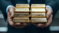 Hands in business suit holding shiny gold bars arranged in two rows, representing wealth, investment and financial success in banking and precious metals market.