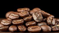 Fresh roasted coffee beans with rich brown color and visible natural texture scattered on dark background, macro photography showing detailed coffee bean structure.