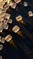 Clear ice cubes scattered on dark wet surface with golden lighting reflections for beverage and cocktail photography backgrounds.