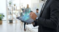 Professional businessman analyzing holographic financial data charts on digital tablet in modern office environment for business analytics and growth strategy.