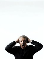 Mature man with gray hair wearing black business suit expressing shock and surprise with hands on head against white background, isolated for commercial and editorial use.