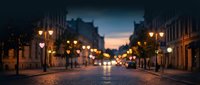 Blurred evening city street with warm glowing streetlights and cobblestone pavement at twilight. Atmospheric urban scene with soft bokeh lights creating dreamy ambiance.