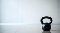 Black kettlebell on white floor against minimalist wall background for fitness training and strength workout equipment concepts.