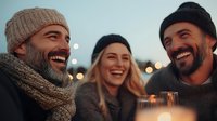 Diverse group of friends laughing and enjoying evening drinks outdoors with bokeh lights and warm candlelight atmosphere creating genuine social connection moment.