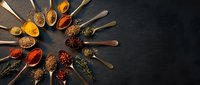 Colorful spices and herbs arranged in wooden spoons on dark slate background. Culinary ingredients for cooking and seasoning food in kitchen.