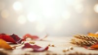 Autumn leaves and wheat ears scattered on wooden surface with warm bokeh lights background for seasonal decoration and harvest celebration.
