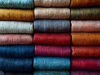 Colorful textile fabric rolls stacked in rows showing various woven patterns and textures for fashion design, upholstery, crafting and interior decoration projects.
