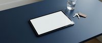 Tablet with blank white screen on dark blue desk beside keys and glass of water, mockup for app or website display.