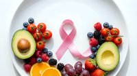 Pink ribbon surrounded by fresh colorful fruits and vegetables on white plate promoting healthy eating and cancer awareness lifestyle.