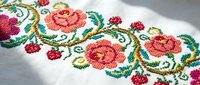 Traditional cross-stitch embroidery with colorful floral pattern on white fabric featuring roses and decorative elements for handicraft and textile design projects.