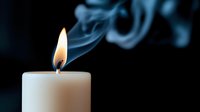 White candle with bright flame and wispy smoke curls against dark background creating atmospheric mood lighting for relaxation and meditation concepts.