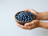 Fresh blueberries in wooden bowl held by hands against white background. Organic fruit for healthy eating, nutrition, and food styling.