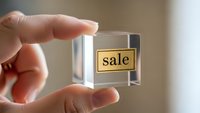 Hand holding transparent glass cube with golden sale label inside for retail marketing and promotional campaigns.