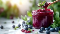 Homemade blueberry jam in glass jar with wooden spoon, fresh berries and mint leaves on rustic table for breakfast and cooking recipes.