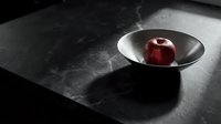 Red apple in metallic bowl on dark textured surface with dramatic lighting, suitable for food photography, still life compositions, and culinary design projects.