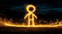 Glowing stick figure made of light trails and sparks standing on illuminated ground against dark night sky, creating magical light painting effect.
