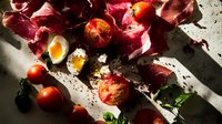Fresh cherry tomatoes and soft boiled eggs scattered among vibrant radicchio leaves on rustic surface with dramatic lighting and shadows, styled for food photography.