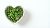 Fresh green arugula leaves in white heart-shaped bowl on clean background for healthy eating and cooking concepts.