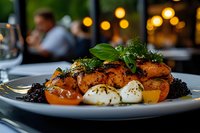 Gourmet salmon fillet with cherry tomatoes, mozzarella and fresh herbs on white plate in upscale restaurant setting with warm ambient lighting.