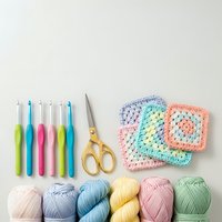 Colorful crochet supplies with yarn balls, hooks, scissors and granny square samples arranged on white background for crafting projects.