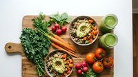 Healthy vegetarian bowls with quinoa, avocado and fresh vegetables on wooden cutting board. Nutritious plant-based meal prep with kale, carrots, tomatoes.
