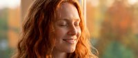 Peaceful redhead woman with closed eyes and gentle smile enjoying warm sunlight, expressing serenity and mindfulness in golden hour lighting.
