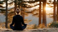 Woman meditating in lotus position during golden hour sunset in peaceful forest setting with warm sunlight filtering through trees creating serene wellness atmosphere.