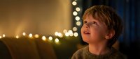 Young blonde boy reading book with warm bokeh lights creating magical evening atmosphere for bedtime stories and childhood education.