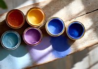 Colorful paint cans with vibrant blue, purple, orange, and red hues arranged on wooden surface with natural sunlight casting artistic shadows.