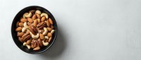 Mixed nuts including almonds, walnuts, and pecans in black bowl on white background for healthy snacking and cooking recipes.