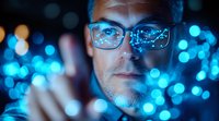 Caucasian male tech professional wearing glasses illuminated by blue digital lights and bokeh effects, representing future technology and innovation in cybersecurity.