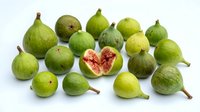 Fresh green figs with one cut open showing pink flesh and seeds, isolated on white background for food and culinary design projects.