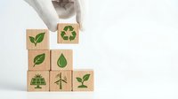 Hand stacking wooden blocks with green eco symbols including recycling, leaves, solar panel and wind turbine representing sustainable business growth.