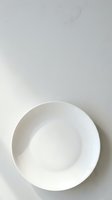 Empty white ceramic bowl on neutral background, overhead view. Minimalist dinnerware for food styling, restaurant menus, culinary blogs, and tableware product displays.