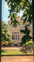 Blooming white tropical flowers frame yellow colonial mansion view through lush green foliage. Dreamy summer garden scene with soft focus background.
