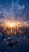 Merry Christmas text written on frosted window glass with ice crystals and warm glowing candlelight in background, winter holiday greeting.