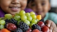 Young diverse children enjoying fresh seasonal fruits including green grapes, blackberries and plums, promoting healthy eating habits and nutrition education.