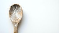 Wooden spoon with flour powder on white background for baking and cooking projects.