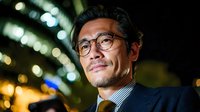 Professional Asian businessman with glasses smiling confidently in modern urban setting with bokeh city lights background for corporate presentations.