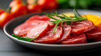 Fresh raw beef slices with rosemary herbs on dark plate, ready for cooking. Premium red meat cuts garnished with green sprig for culinary preparation.