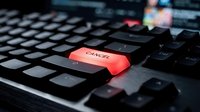 Red cancel button glowing on black computer keyboard in dark office environment for business technology and data management concepts.