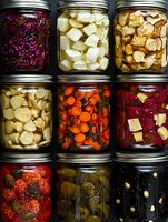 Assorted colorful pickled and fermented vegetables in glass mason jars arranged in rows, including cabbage, carrots, radishes and cucumbers. Food preservation concept.