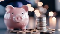 Pink piggy bank with stacked coins on wooden surface against warm bokeh lights background for savings and financial planning concepts.