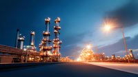 Oil and gas refinery plant with illuminated industrial equipment at dusk, dramatic sky with glowing street lights creating industrial atmosphere.