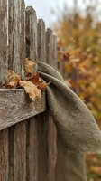 Rustic burlap sack draped over weathered wooden fence with autumn leaves scattered around creating cozy fall harvest atmosphere for seasonal decorating.
