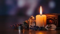 Mystical candle flame illuminates crystals, dried herbs and ornate wooden box creating atmospheric spiritual meditation scene for wellness practices.