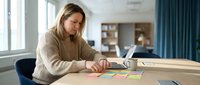 Young blonde businesswoman analyzing colorful charts and graphs at modern office desk with laptop for strategic planning and data review.