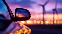 Side mirror reflection captures dramatic sunset with wind turbines and bokeh lights, creating atmospheric scene of sustainable energy and modern transportation.