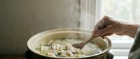 Senior woman cooking homemade pasta with herbs in kitchen pan, stirring traditional Italian meal preparation for family dinner at home.